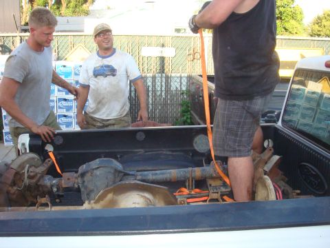 1992 Ford Bronco - Three men are seen in and around the bed of a pickup truck, which is loaded with axles and other parts.