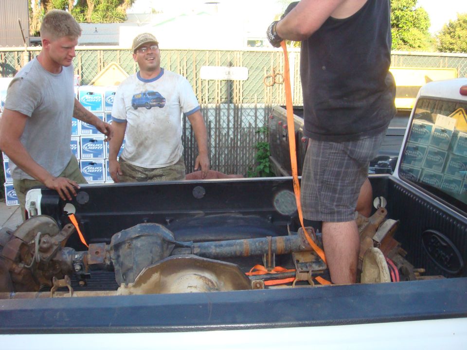 Pickup truck bed loaded with axles and three men