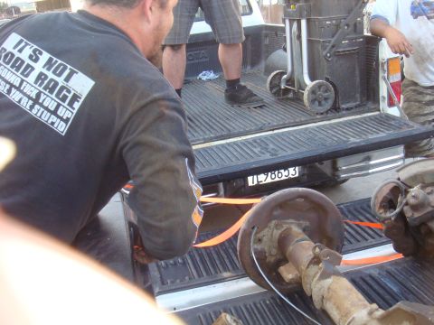 1992 Ford Bronco - Two axles are being loaded into the bed of a pickup truck by several people.