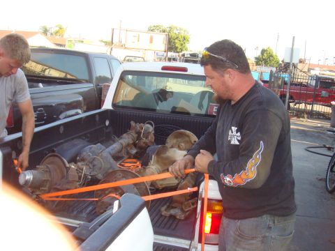1992 Ford Bronco - Axles are loaded into the bed of a pickup truck, secured with orange straps.