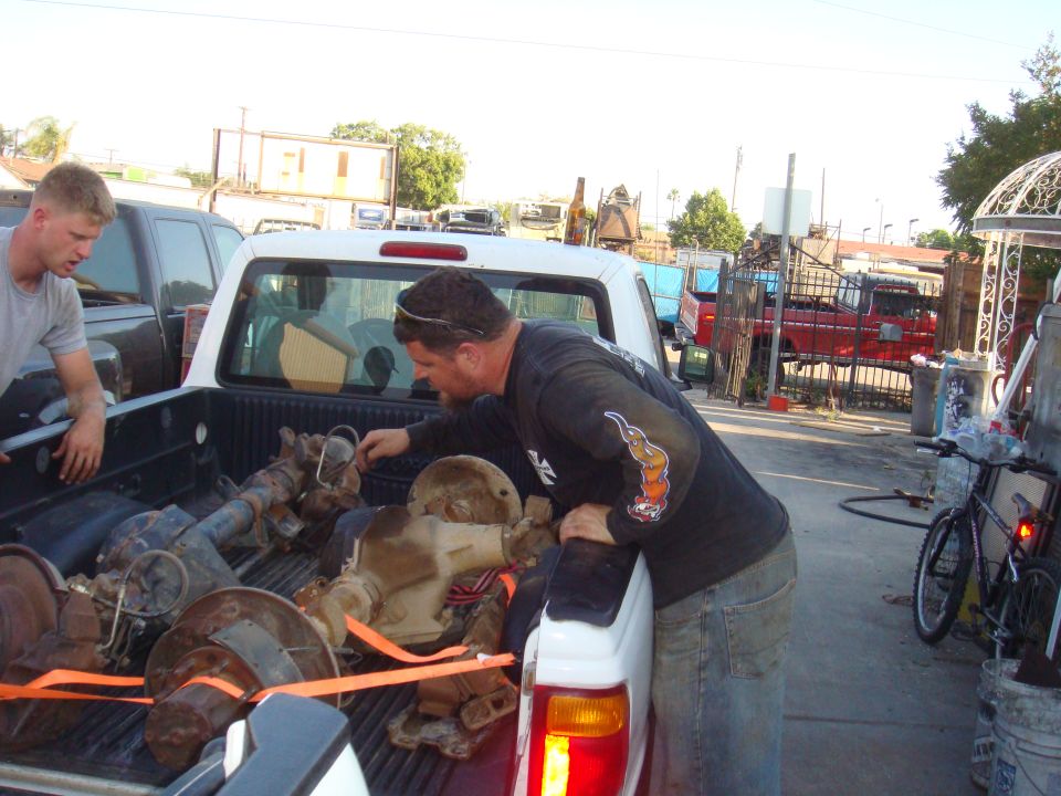 Pickup truck bed loaded with axles and differentials. Two men are visible