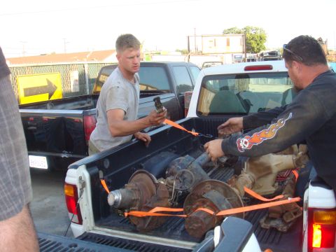 1992 Ford Bronco - Men are loading axles into the bed of a white pickup truck.