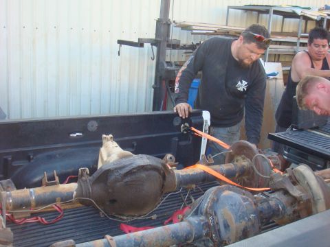 1992 Ford Bronco - Several old vehicle axles are being loaded into the back of a pickup truck by a group of men.