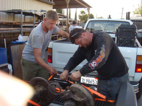 1992 Ford Bronco - Two men work in the bed of a white pickup truck, securing large mechanical parts with straps.