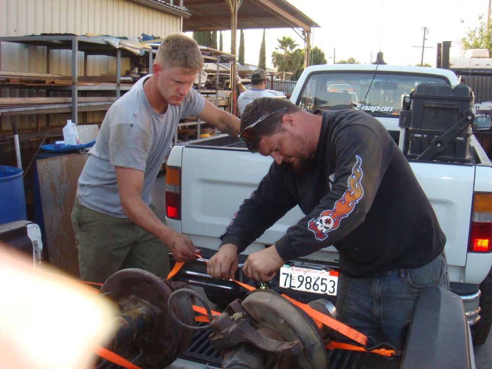 Truck bed with two men securing parts with orange straps. California license plate 7L98653 is visible