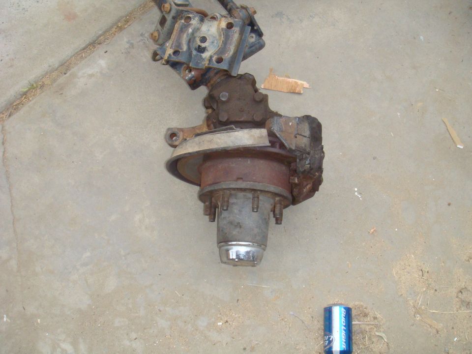 Rusty front axle assembly with brake drum and hub, lying on concrete