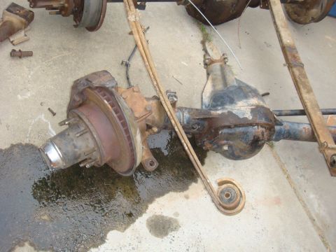 1992 Ford Bronco - Disassembled vehicle axles and leaf springs are laid out on a concrete surface, showing parts of the suspension system.