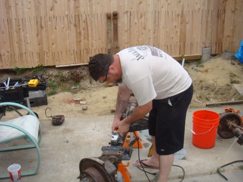 1992 Ford Bronco - A person is using an angle grinder on a vehicle axle assembly that is supported by orange jack stands.