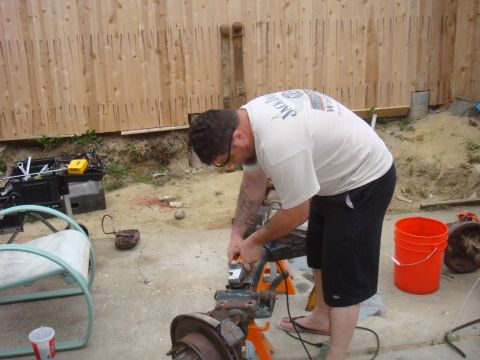1992 Ford Bronco - Man grinding on a vehicle axle assembly outdoors.