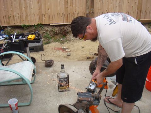 1992 Ford Bronco - A man is using an angle grinder on a metal part outdoors, with a bottle of whiskey and tools around.