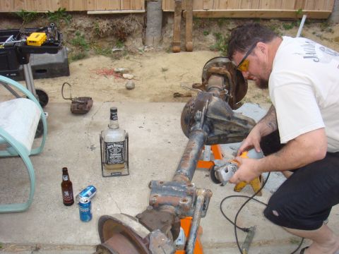 1992 Ford Bronco - A man works on a vehicle axle assembly outdoors, with a bottle of Jack Daniels and beer nearby.