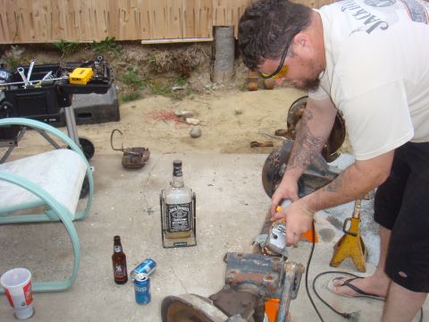 1992 Ford Bronco - A man uses an angle grinder on a vehicle axle, with a bottle of Jack Daniels and beer cans on the ground.