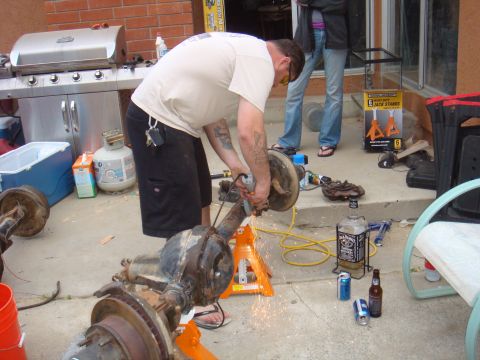 1992 Ford Bronco - Man working on a vehicle axle with an angle grinder, sparks flying.