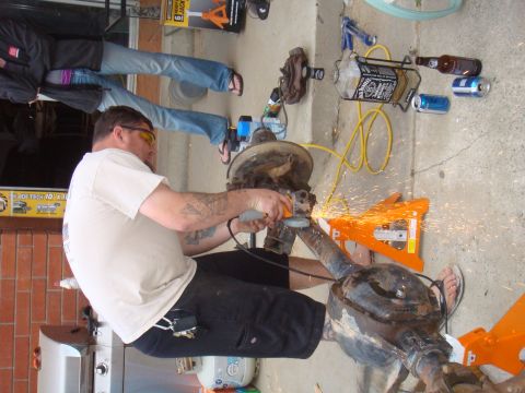 1992 Ford Bronco - A man uses an angle grinder on a vehicle axle while sparks fly. Other people are visible in the background.