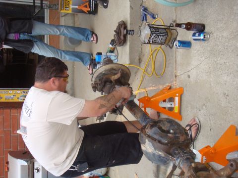 1992 Ford Bronco - A man grinds on a car axle assembly supported by orange jack stands.