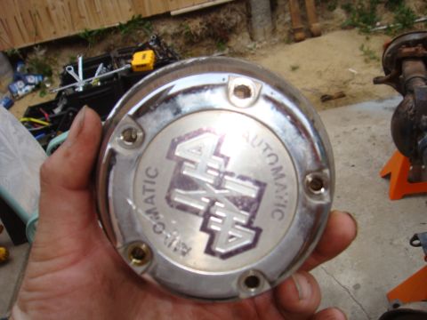 1992 Ford Bronco - A chrome hubcap with '4x4 AUTOMATIC' is held in a hand, with tools and a vehicle axle visible in the background.