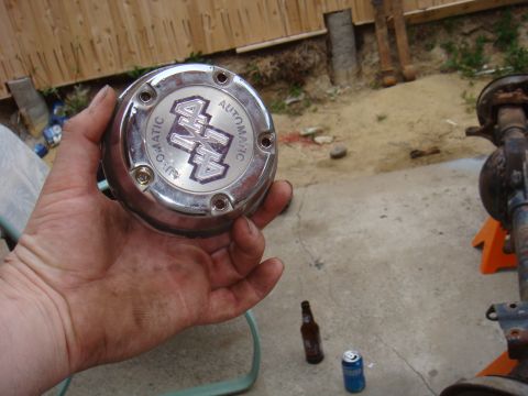 1992 Ford Bronco - A person holds a chrome hubcap with '4x4 AUTOMATIC' text, with a vehicle axle assembly visible in the background.