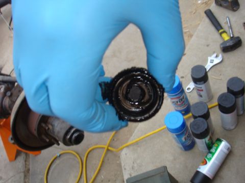 1992 Ford Bronco - A gloved hand holds a greasy bearing assembly, with various spray cans and tools scattered on the ground, suggesting a repair or maintenanc…