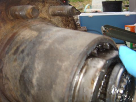 1992 Ford Bronco - Close-up of a rusty wheel hub assembly with exposed gears and a blue gloved hand.