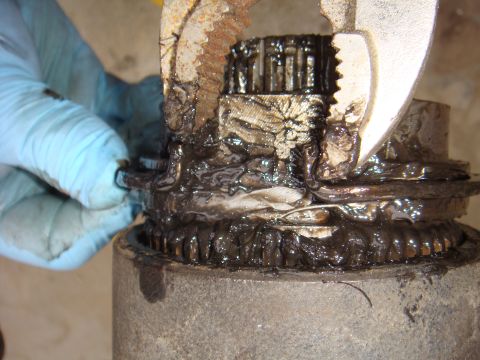 1992 Ford Bronco - A close-up view of a greasy axle component being manipulated with a wrench and a gloved hand.