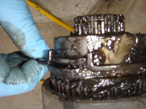 1992 Ford Bronco - Close-up of a greasy axle component, with blue-gloved hands manipulating it. Text 'SUPERMOTORS' is visible at the bottom.