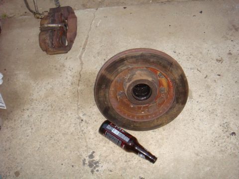 1992 Ford Bronco - A brake rotor and caliper sit on a concrete surface next to a bottle of beer.