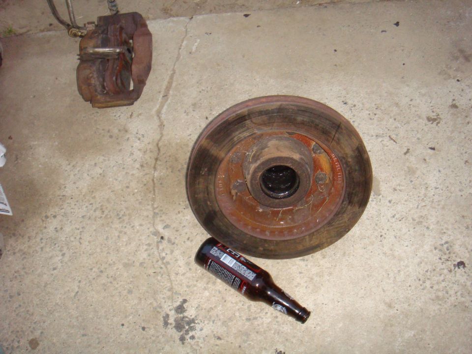 Brake rotor and caliper on concrete floor next to a beer bottle