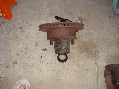 1992 Ford Bronco - A rusty brake rotor and hub assembly sits on a concrete floor next to a beer bottle.