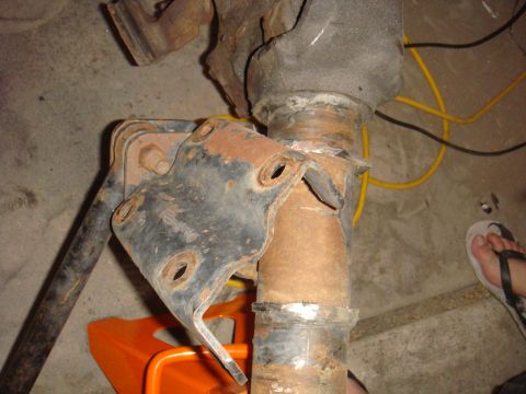 1992 Ford Bronco - Close-up of a heavily rusted axle component with a bracket, resting on an orange jack stand.