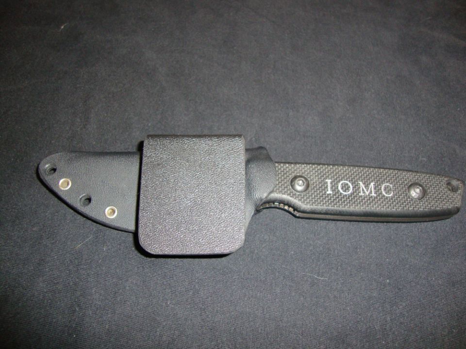 Black fixed-blade knife in a Kydex sheath with IOMC marked on the handle