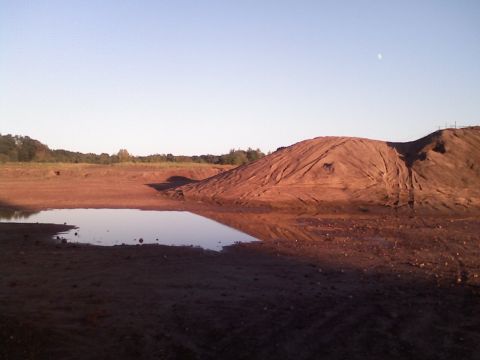 1994 Ford Bronco - A desolate scene with a large dirt mound and a reflective puddle under a clear sky.