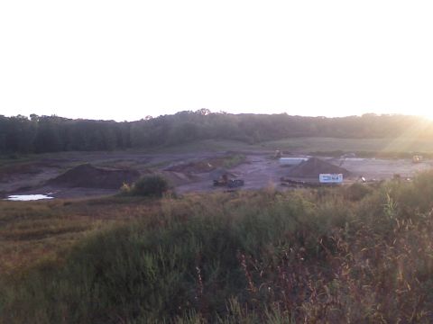 1994 Ford Bronco - A construction site with various pieces of heavy equipment and dirt mounds is visible under a bright sky.