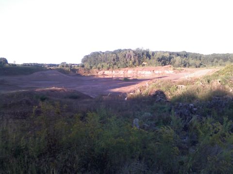 1994 Ford Bronco - A wide view of a desolate quarry with rough terrain and distant trees under a bright sky.