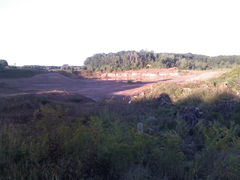 Open dirt pit riding area with graded banks, brush and tree line, no vehicle visible