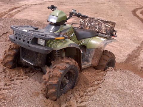 1994 Ford Bronco - An all-terrain vehicle is stuck in a muddy ditch, with its tires caked in dirt.