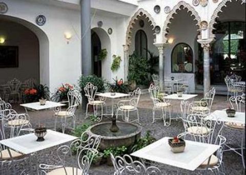 1991 Ford LTD Crown Victoria - An outdoor courtyard features white wrought iron tables and chairs surrounding a central fountain, with decorative arches and potted plants.