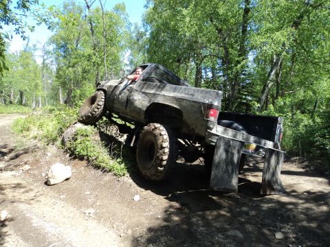 1990 Chevrolet Suburban - This heavily modified truck navigates a challenging off-road course with large, aggressive tires.