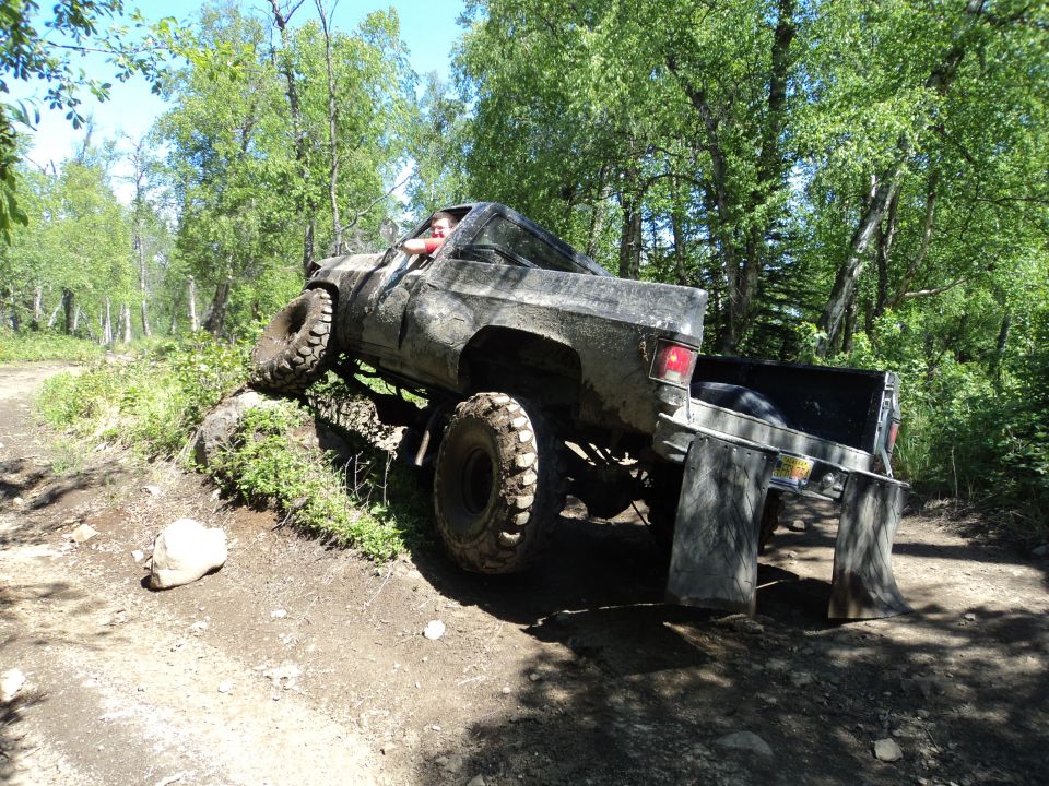 Muddy lifted truck with large tires on a dirt trail, driver visible