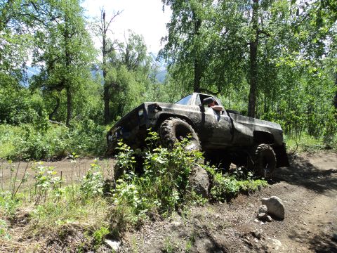 1990 Chevrolet Suburban - This heavily modified pickup truck navigates a challenging off-road course, its build evident despite the mud.