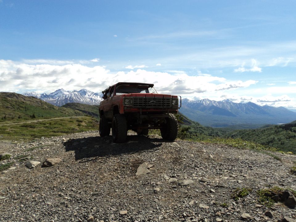 Red off-road SUV parked on a gravelly hill with mountains in the background