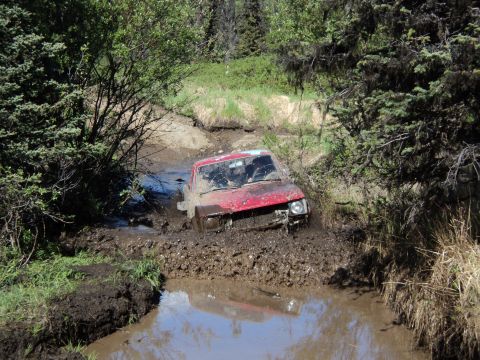 1990 Chevrolet Suburban - Off-roading adventure goes wrong as a red SUV gets stuck in thick mud.