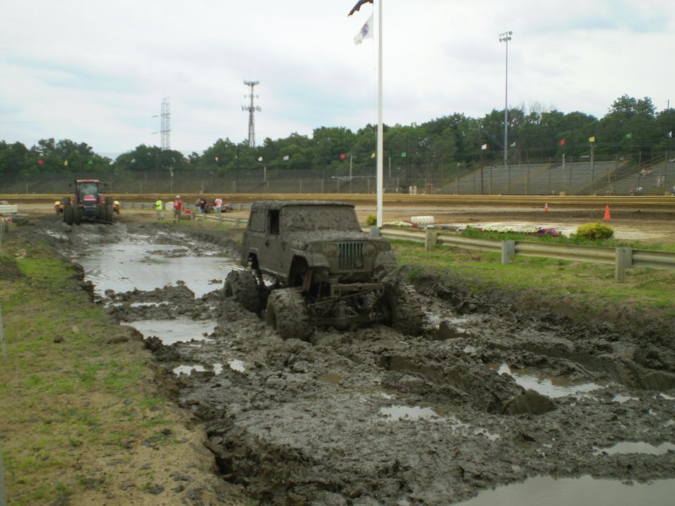 Mud-covered Jeep Wrangler stuck in a mud pit with a tractor in the background