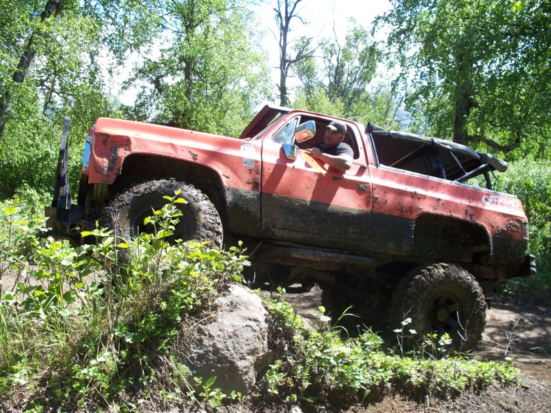 Red off-road truck with large tires navigating a rocky trail, mud splattered on its body
