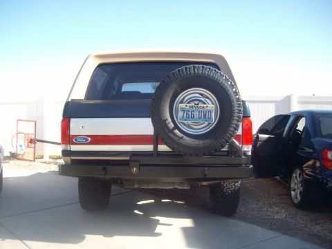 1993 Ford Bronco - Rear view of a two-tone dark blue, silver and red Ford Bronco with a tan hardtop, fitted with a heavy plate-steel rear bumper and swing-out…