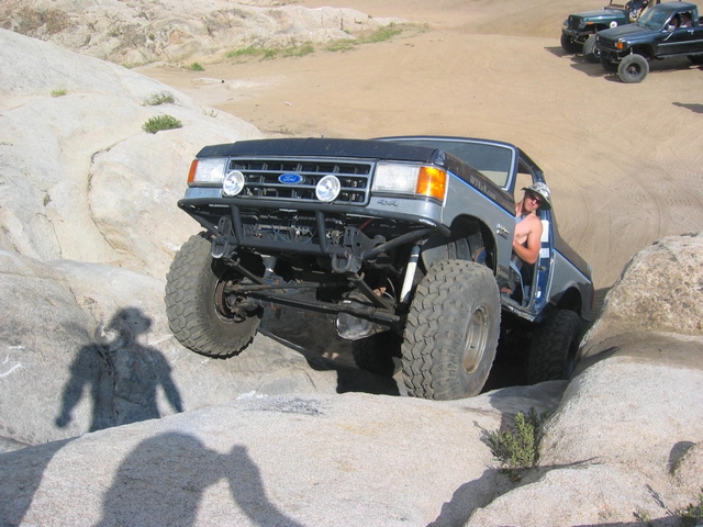 Lifted blue Ford Bronco climbing boulders with front axle exposed