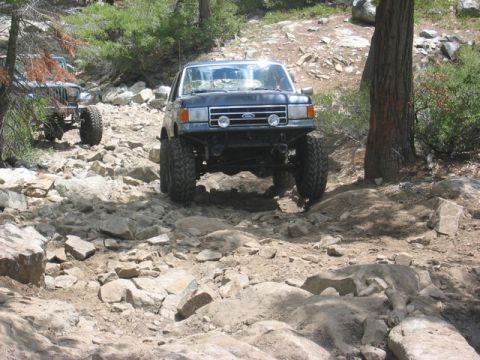 1989 Ford Bronco - A dark blue Ford Bronco navigates a challenging rocky terrain on an off-road trail.