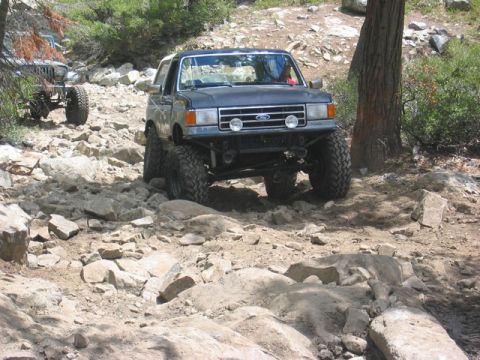 1989 Ford Bronco - This lifted 1989 Ford Bronco tackles a challenging rocky terrain, with another off-road vehicle visible in the background.