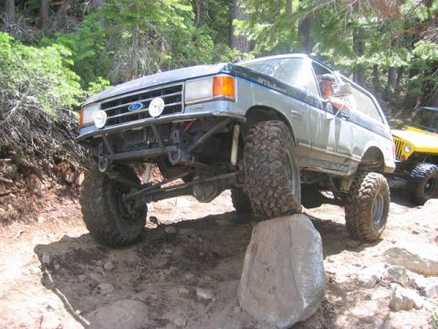 1989 Ford Bronco - Modified Ford Bronco navigating an off-road obstacle with a yellow Jeep nearby.