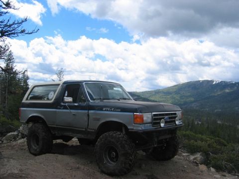 1989 Ford Bronco - This lifted 1989 Ford Bronco navigates a rocky trail, its off-road capabilities against a scenic mountain backdrop.