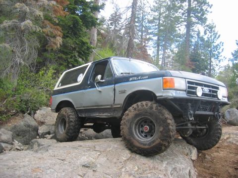 1989 Ford Bronco - This modified Ford Bronco navigates a rocky, wooded terrain with its large off-road tires.